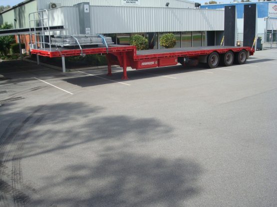 drop deck trailer in red standing in parking lot in front of store front