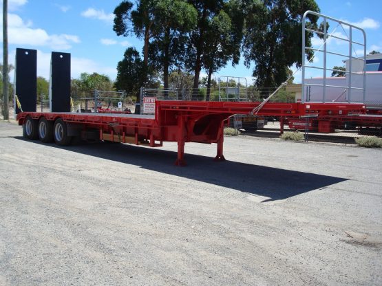 drop deck trailer not hooked onto truck in red standing in shop yard