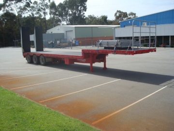 drop deck trailer not hooked onto truck in red standing in parking lot